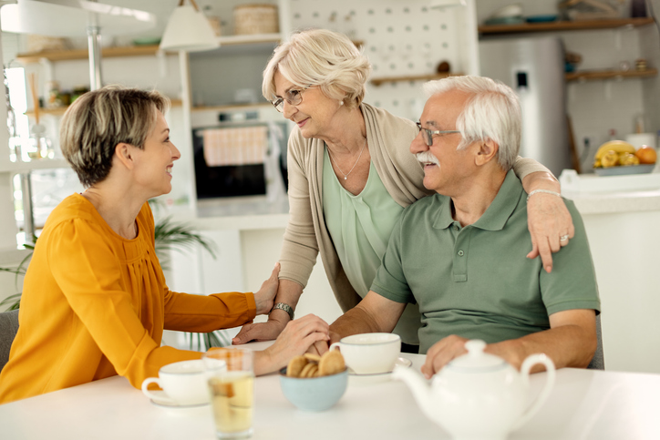 Older adult couple engages in conversation with adult daughter at table.