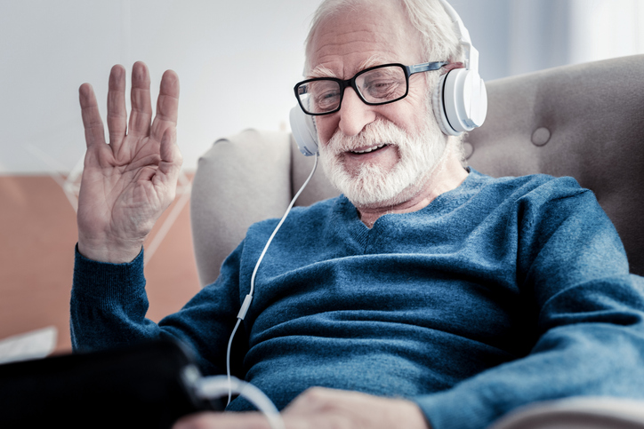 Positive nice joyful man smiling and waving his hand while greeting his family on a screen