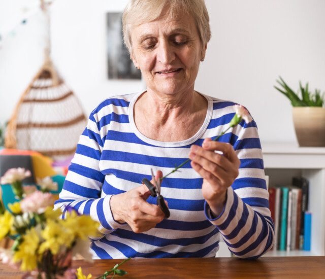 Older woman puts together a beautiful yellow flower arrangement for her living space